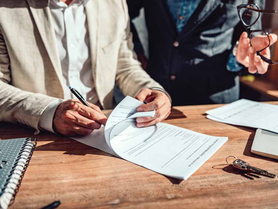 A buyer and seller signing documents at a desk with a business broker present during a small business purchase