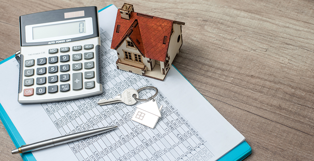 A calculator sits next to a house keychain on a table, suggesting mortgage budgeting.