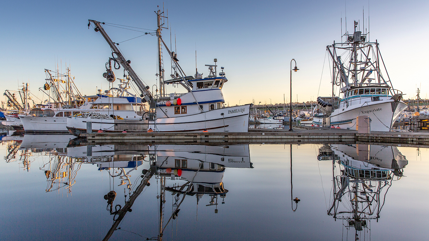 A commercial fishing boat tied up at a dock in winter, with nets and gear on deck.