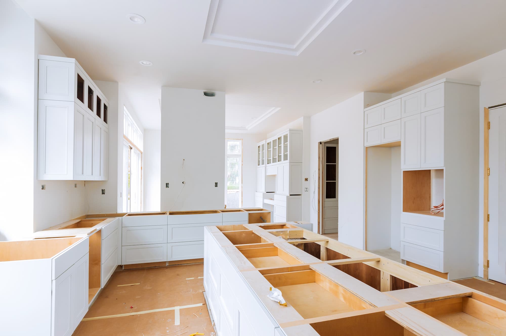 A contractor measuring kitchen cabinets during an in-progress home renovation, with tools and lumber visible in a real home