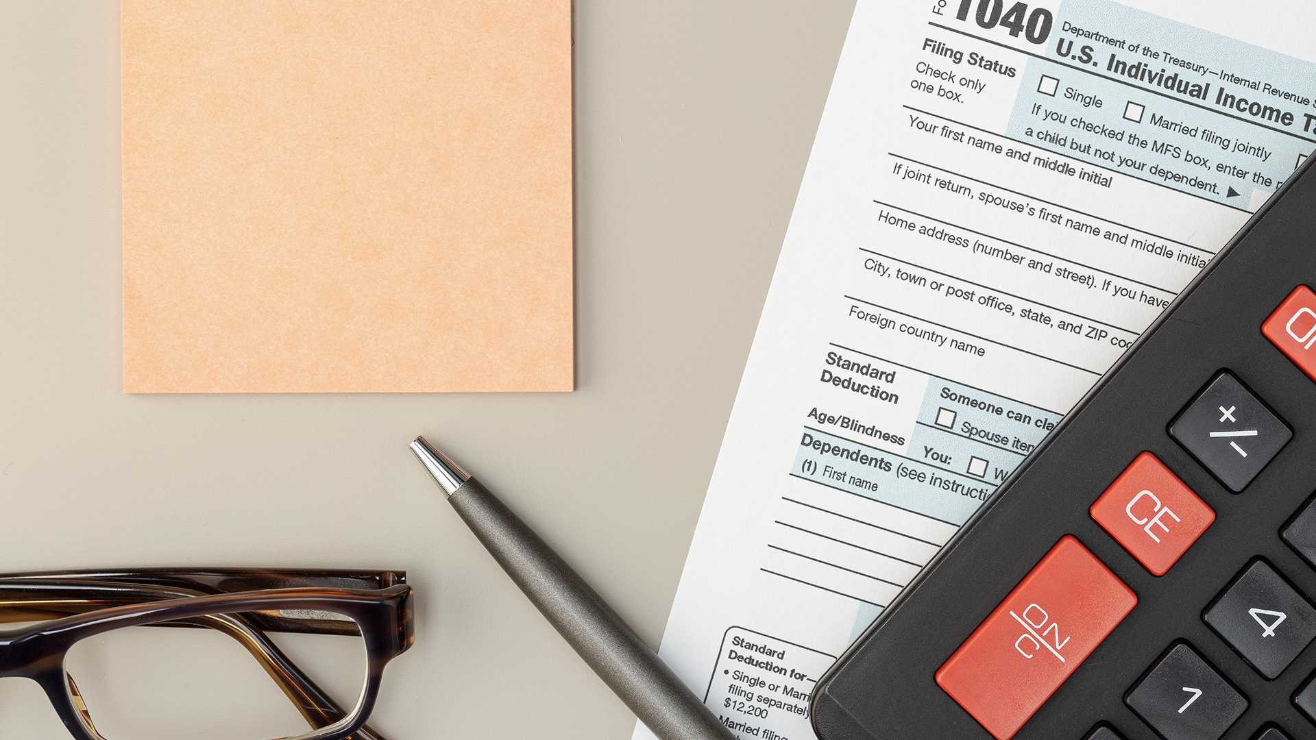 A desk with a calculator, check stubs, and tax forms spread out as a business owner prepares payroll paperwork