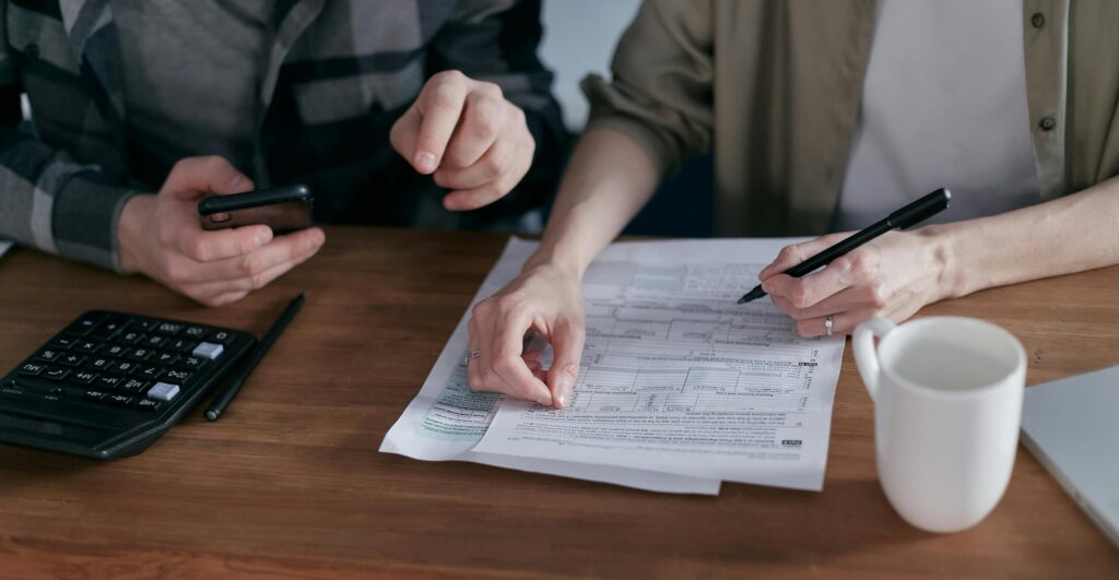 A desk with printed bank statements, a calculator, and a business owner’s hands highlighting transactions