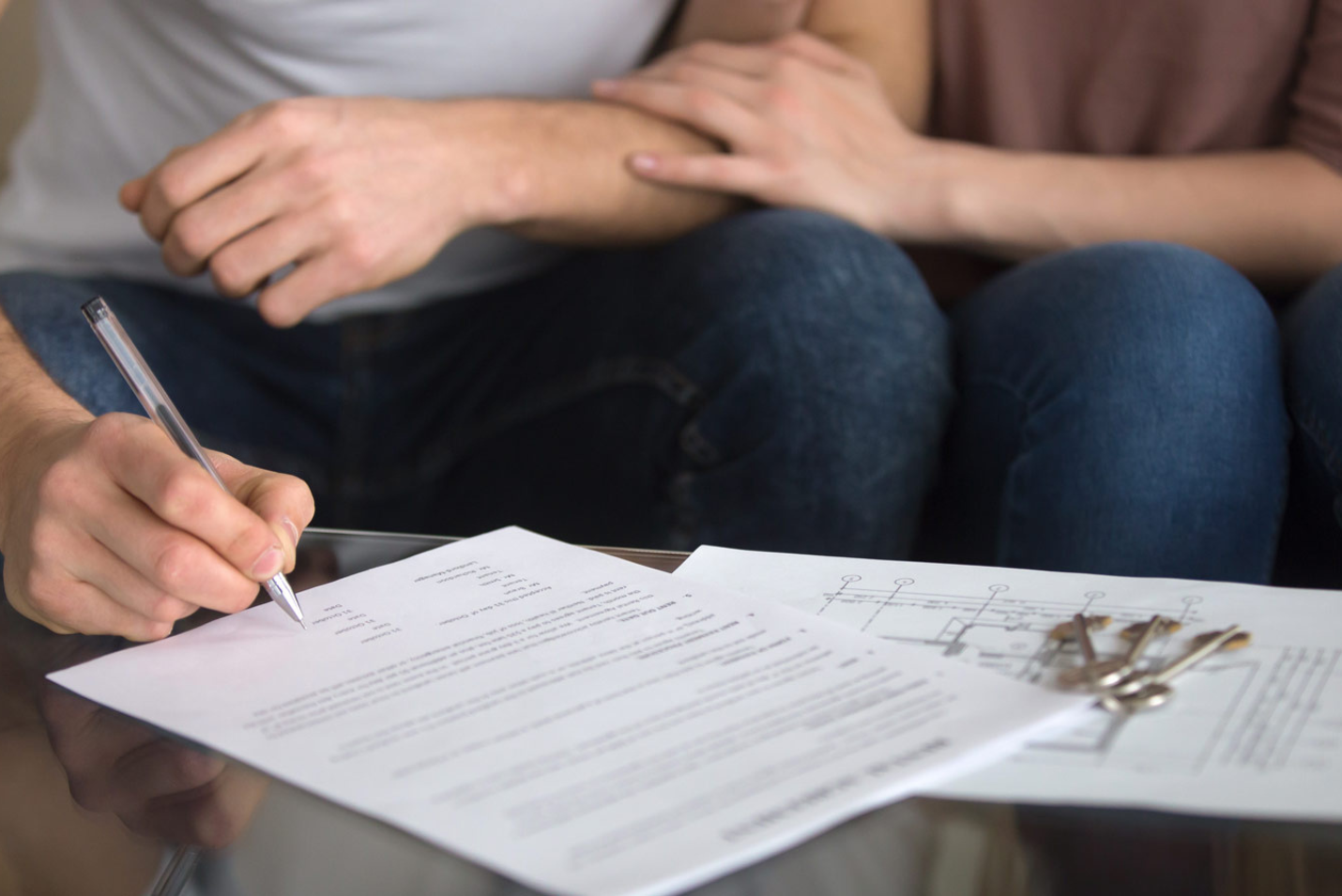 A homeowner signing loan documents at a dining table next to a folder labeled for home financing