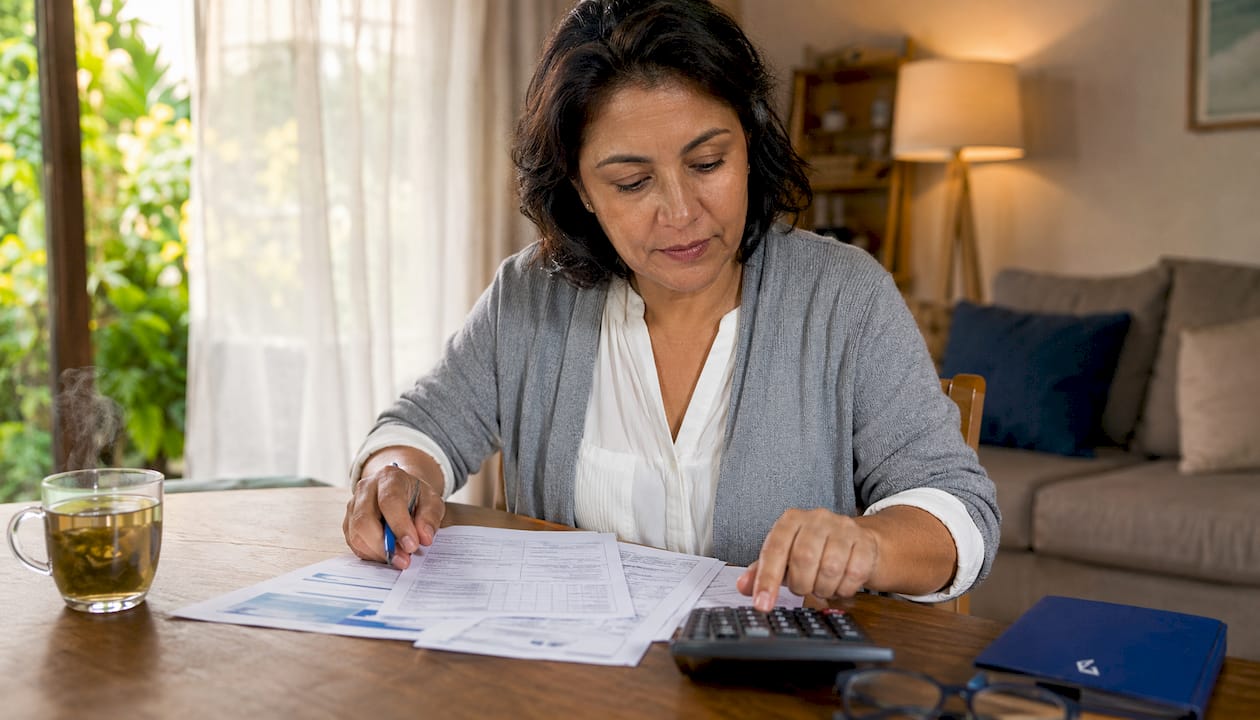 A homeowner sitting at a dining table reviewing loan documents and a laptop budget spreadsheet in a well-lit home