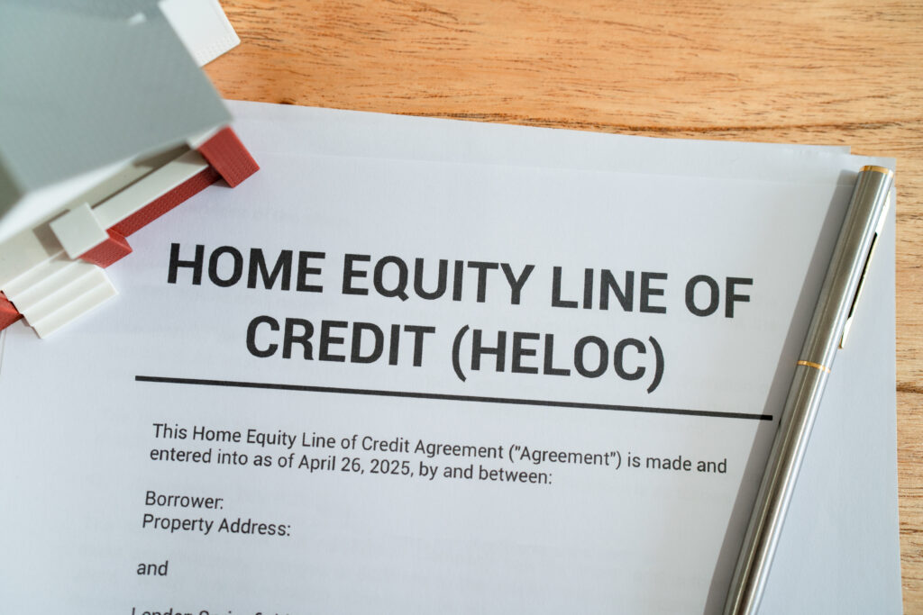 A homeowner sitting at a kitchen table reviewing loan documents and a laptop budget spreadsheet, with a pen and calculator nearby
