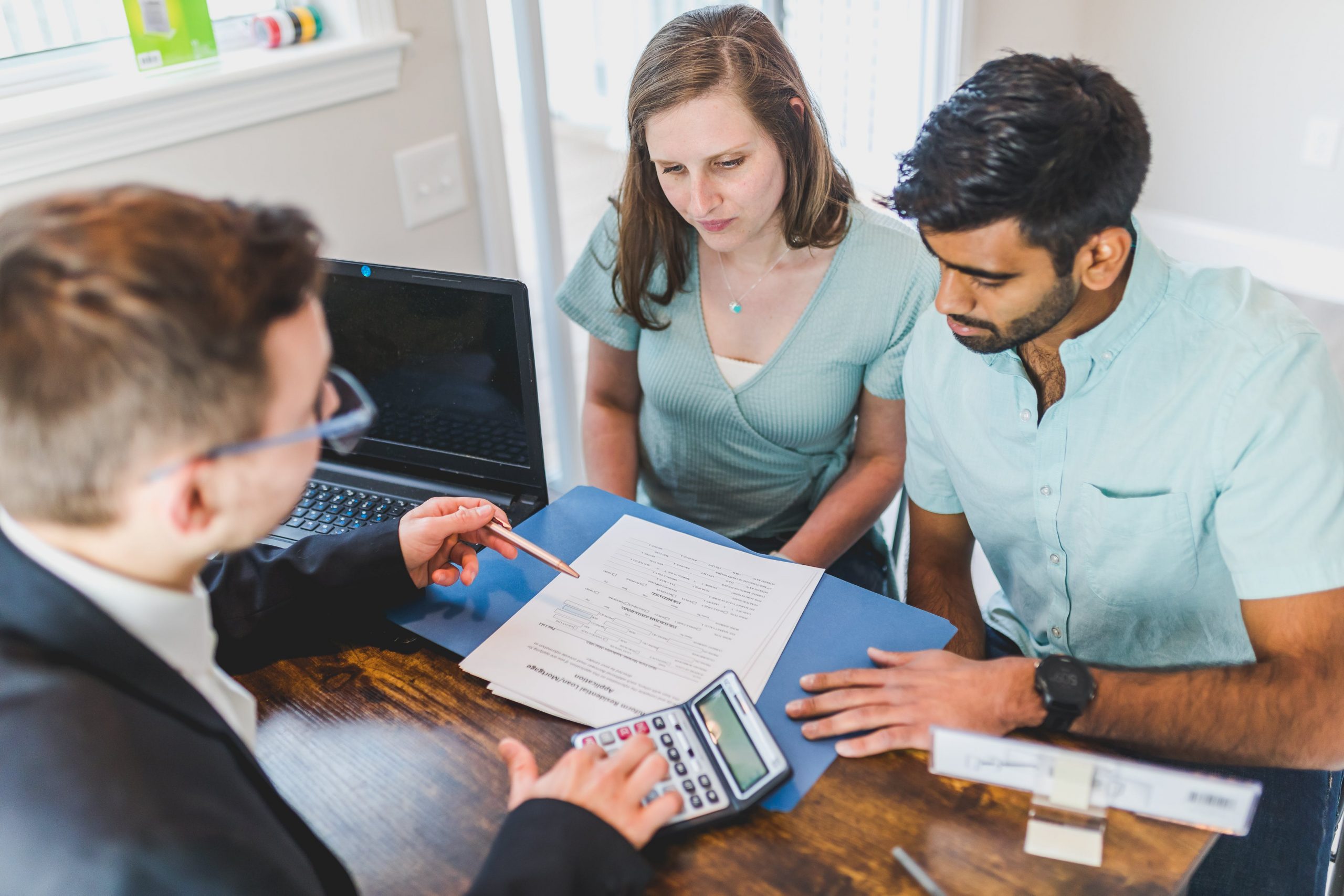 A mortgage loan officer meeting with a couple at a desk, reviewing printed loan estimates and a calculator