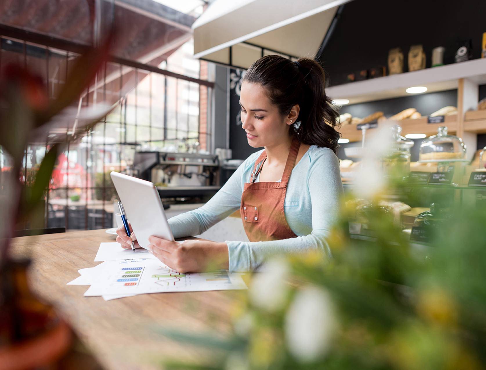 A small business owner at a desk reviewing a vendor invoice and preparing an online payment on a laptop in a real office setting