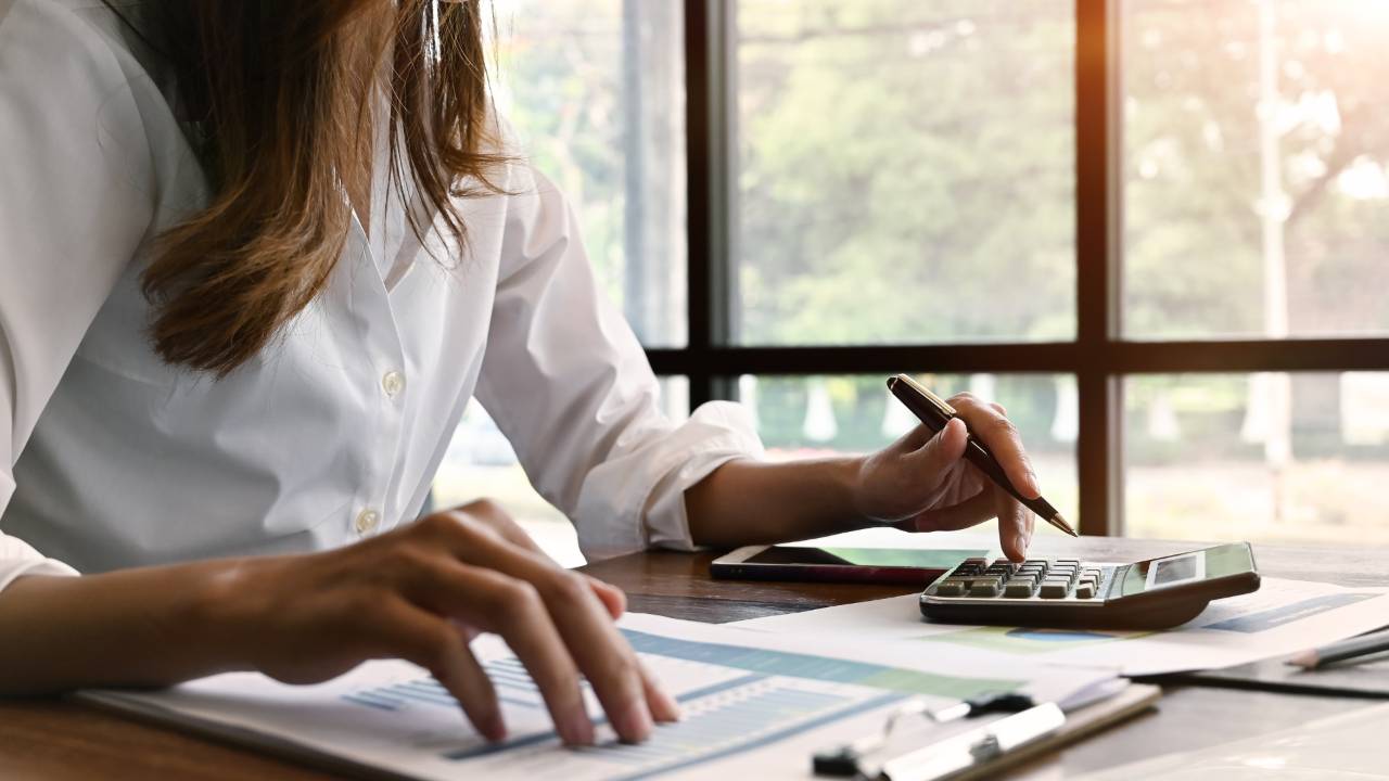 A small business owner at a home office desk organizing tax returns, bank statements, and a laptop with accounting software open