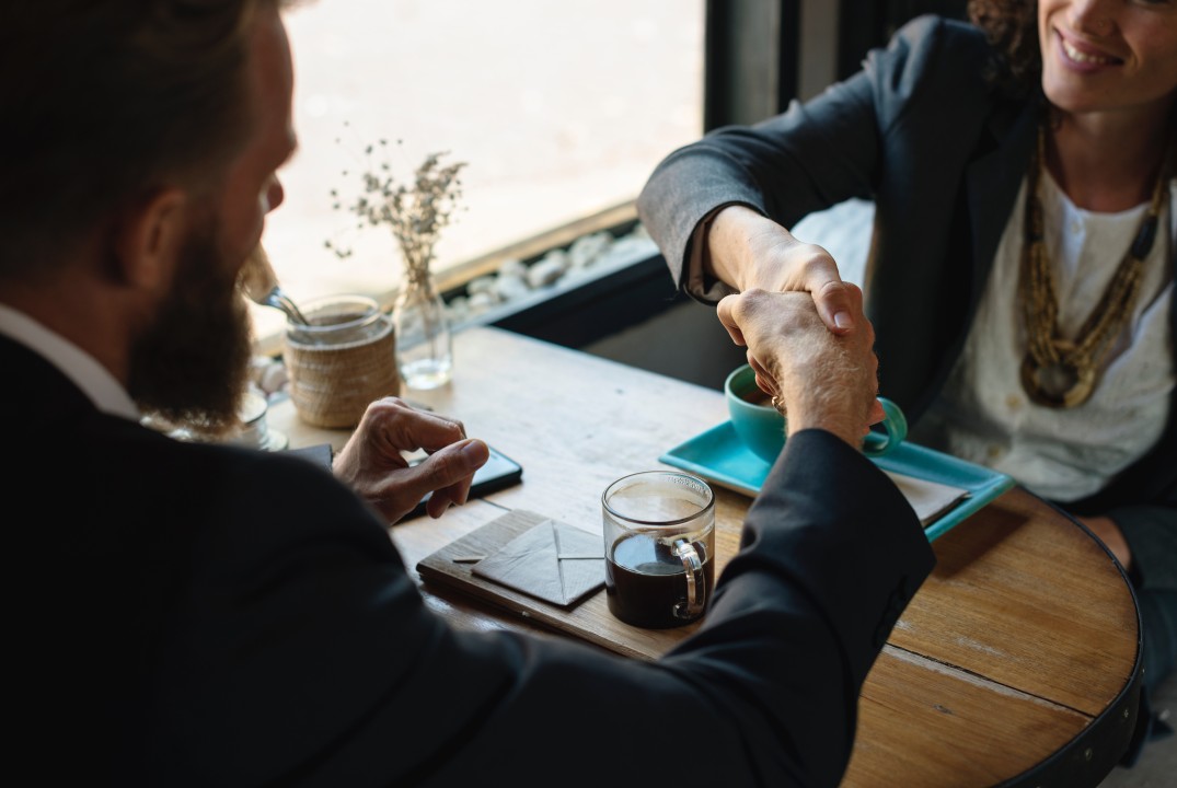 A small business owner meeting with a professional at a coffee shop table with a laptop open and documents on the table