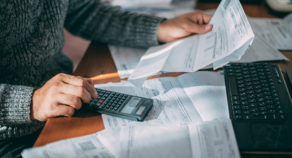 A small business owner sitting at a desk reviewing printed invoices and a laptop spreadsheet in a modest office, natural daylight