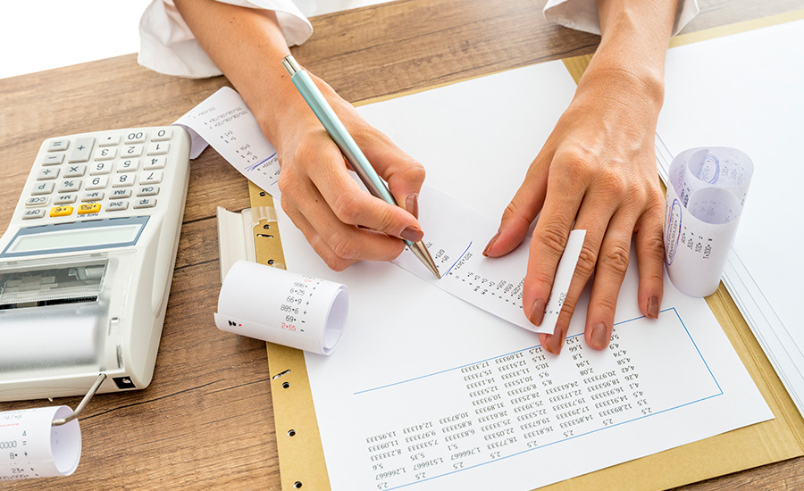A small business owner sitting at a desk reviewing paper receipts and a calculator next to a laptop, candid real-life photography