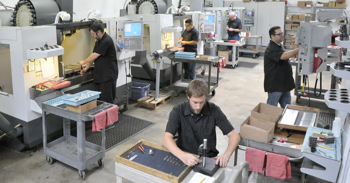 A small manufacturing business owner walking through a workshop floor near a CNC machine and workbenches