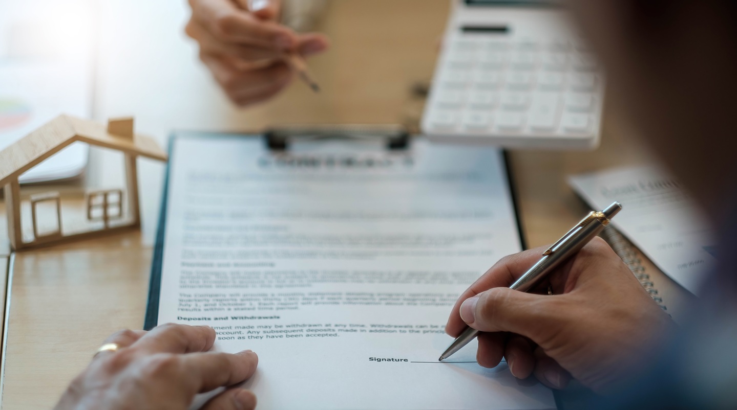A veteran homeowner reviewing and signing refinance paperwork at a dining table with a partner nearby, realistic candid photograph